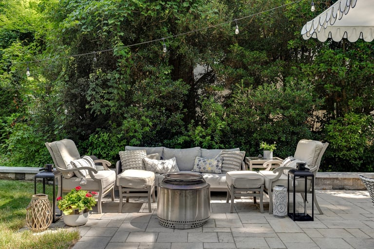 Cozy outdoor seating arrangement with cushioned chairs, fire pit and lush greenery
